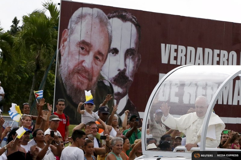 Pope Francis greets believers while he passes in front of a billboard with and image of Cuba’s former leader Fidel Castro and Cuban independence hero Jose Marti, outside the airport in Havana