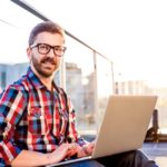 storyblocks/Young businessman writing on a laptop computer, sitting on the balcony