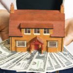 storyblock/A person holding a miniature house and some dollar bills for making payments