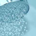 freepik/Closeup of a shower head with sprinkling water, blue toned photo.