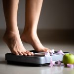 freepik/female-leg-stepping-weigh-scales-with-measuring-tape-apple_53476-4005