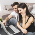 smiling-young-couple-using-laptop-home_23-2148137469