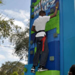 Joshua, a blind or visually impaired client, scales a rock-climbing wall.