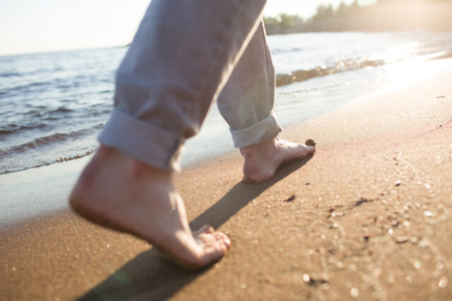 Feet of man walking down wet sand along coastline in the morning Asset ID: SBI-325331464