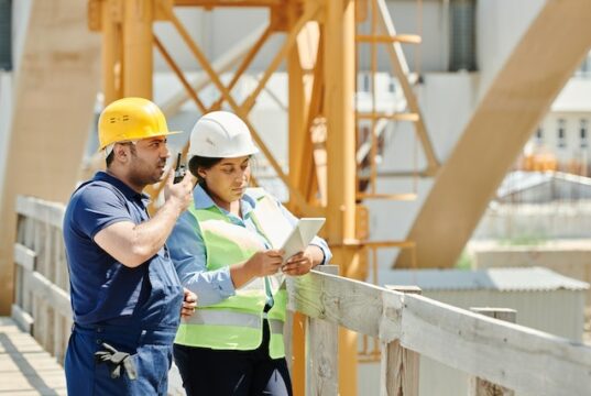 https://www.pexels.com/photo/a-man-in-blue-shirt-using-a-walkie-talkie-while-standing-beside-the-woman-near-the-wooden-fence-8961131/
