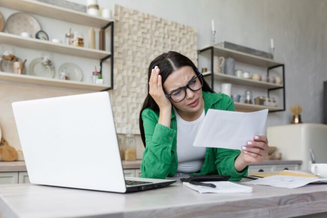 A woman working at home with a laptop. She holds a letter, a document in her hand https://www.freepik.com/premium-photo/shocked-young-woman-working-kitchen-table-with-laptop-she-holds-letter-document-her_36993970.htm#page=2&query=bad%20letter&position=10&from_view=search&track=sph
