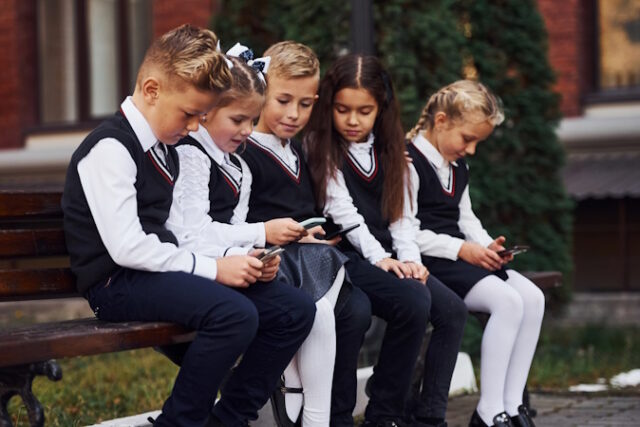 School kids in uniform that sits outdoors on the bench with smartphones. https://www.vecteezy.com/photo/15243891-school-kids-in-uniform-that-sits-outdoors-on-the-bench-with-smartphones