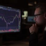 Man analyzing stock market data on computer screen in dark setting