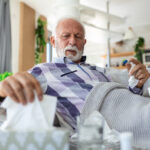Sick elderly man checking his temperature suffering from seasonal flu or cold lying on sofa caughing suffering from seasonal flu or cold. . Ill senior feel unhealthy with influenza at home