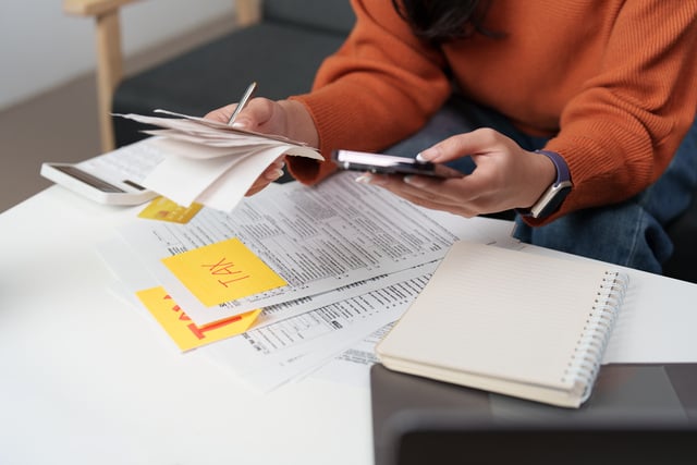 Tax management. Individual using smartphone while organizing tax documents. https://www.vecteezy.com/photo/73228596-tax-management-individual-using-smartphone-while-organizing-tax-documents