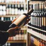 Faceless Person Holds Taking from Shelf Bottle of Wine in Store, Close up